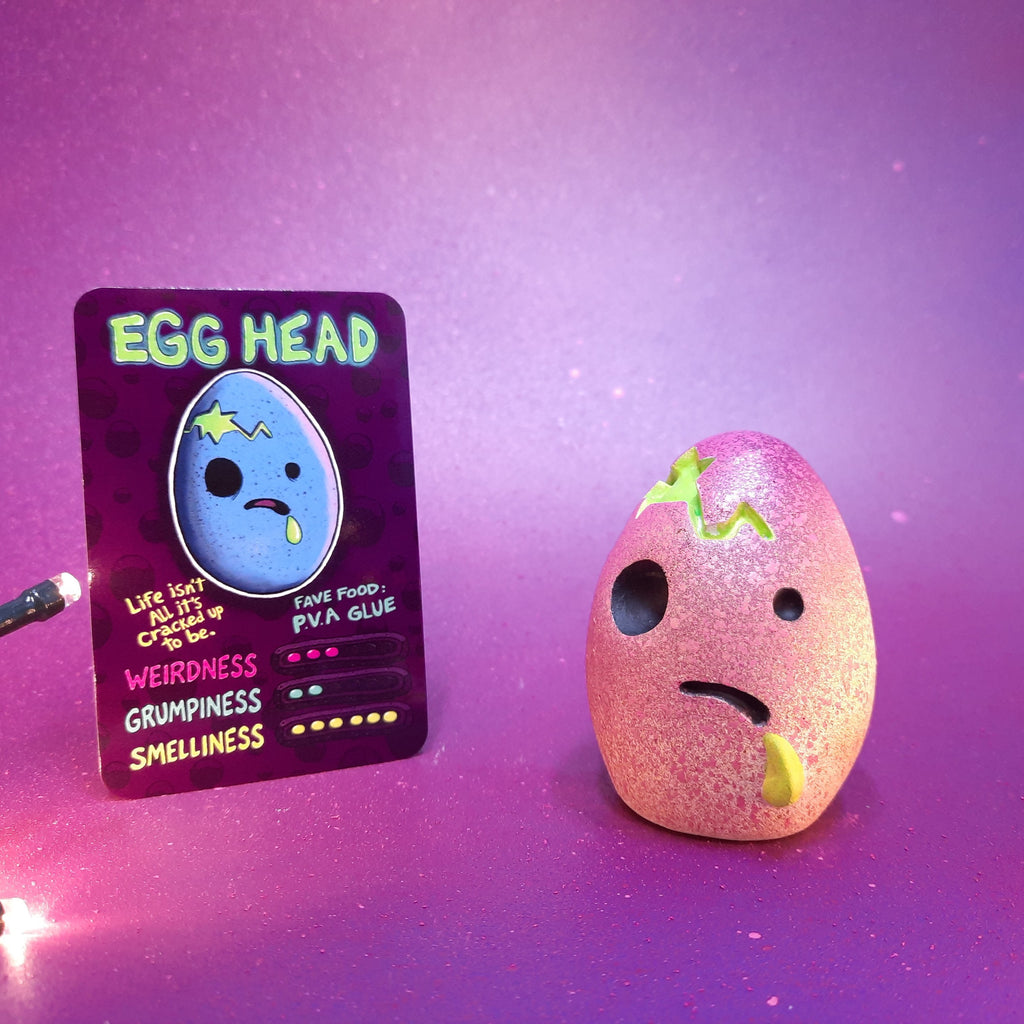 Pink textured 'Egg Head' toy with a matching card on a purple background